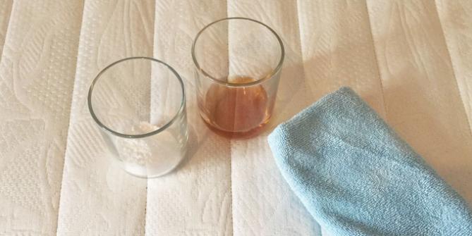 Ein Glas Backpulver, ein Glas mit Essig und ein Putzlappen auf Matratze